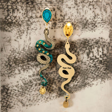Load image into Gallery viewer, Pair of snake-shaped clip-on earrings with turquoise and gold design on a snake skin background