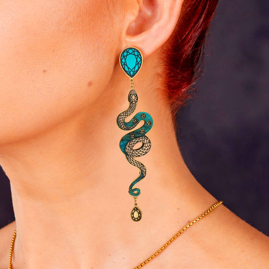 Teal snake-shaped earring worn by a person with a blurred dark background