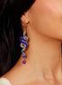 Close-up of a woman wearing a snake-shaped earring with a purple gemstone against a purple background