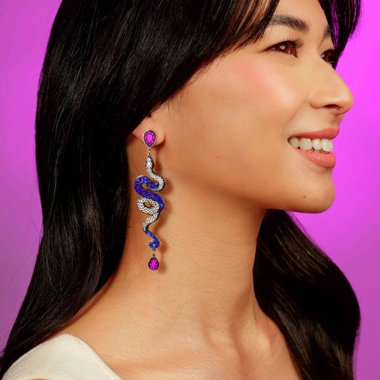 Woman wearing a unique earring with a purple gemstone on a purple background
