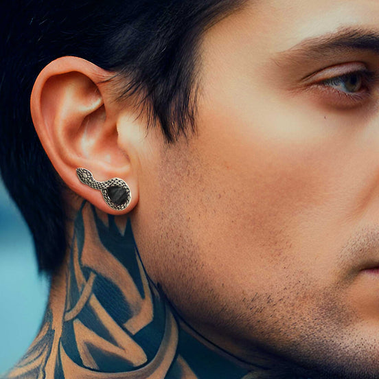 Close-up of a man's ear with a black earring, showcasing tattooed neck.