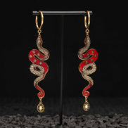 Red and gold Snake-shaped earrings on a black stand with a dark textured background