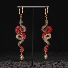 Load image into Gallery viewer, Red and gold Snake-shaped earrings on a black stand with a dark textured background