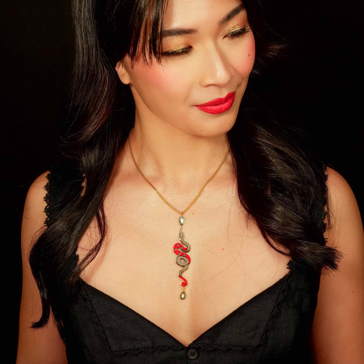 Woman wearing a black dress and a necklace with a red pendant against a dark background