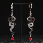 Pair of silver snake-shaped black earrings with red gemstones on a black stand.