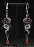 Pair of silver snake-shaped black earrings with red gemstones on a black stand.