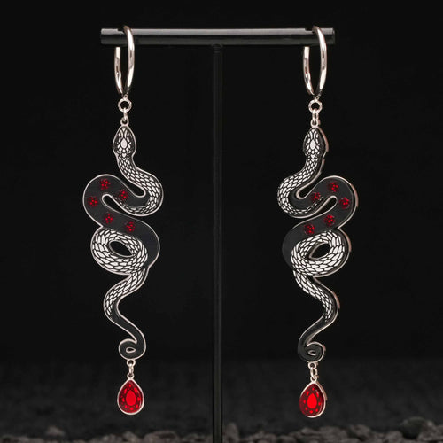 Pair of silver snake-shaped black earrings with red gemstones on a black stand.