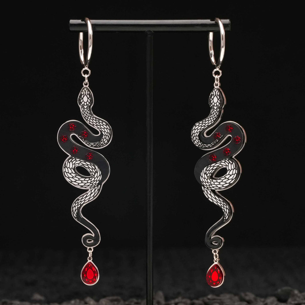 Pair of silver snake-shaped black earrings with red gemstones on a black stand.