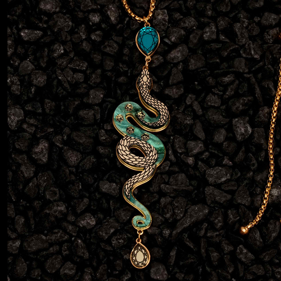 Decorative snake-shaped pendant with turquoise and gold elements on a dark textured background