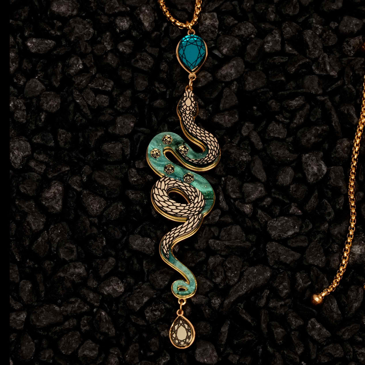 Decorative snake-shaped pendant with turquoise and gold elements on a dark textured background