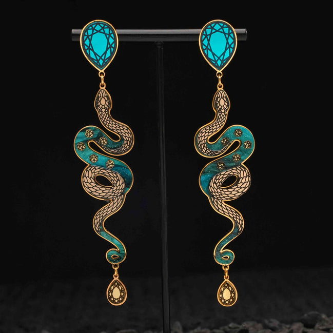 Pair of snake-shaped earrings with turquoise and gold design on a black background