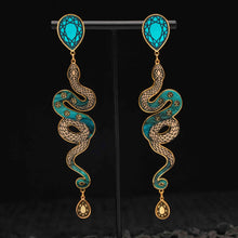 Load image into Gallery viewer, Pair of snake-shaped earrings with turquoise and gold design on a black background