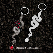 Pair of snake-shaped hoop earrings on a dark textured background with text 'Embedded in Stainless Steel'.