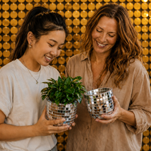 Load image into Gallery viewer, Two women smiling and holding small green potted plants in mirrored silver planters, standing in front of a gold sequin wall.