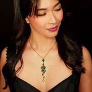 Woman wearing a black top and a necklace with a green pendant against a dark background