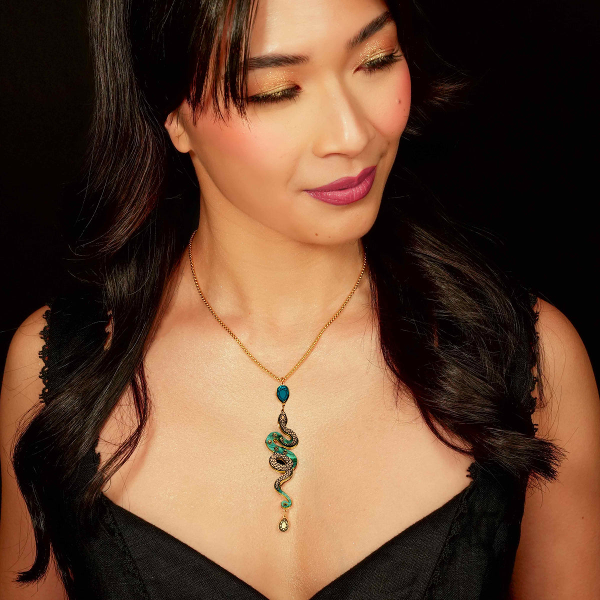 Woman wearing a black top and a necklace with a green pendant against a dark background